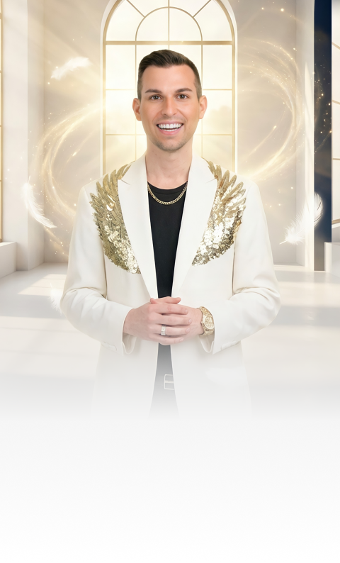 Matt Fraser, wearing a white jacket with gold wing patterns, smiles in a bright room with large windows and floating feathers.