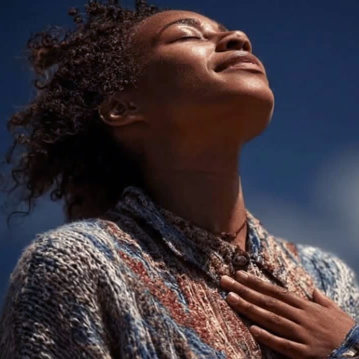 Matt Fraser stands outdoors with eyes closed and hand on chest, wearing a textured sweater and facing upwards toward sunlight.