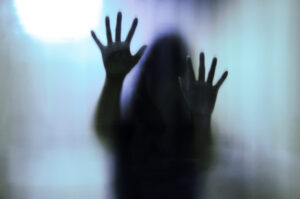 A blurry silhouette of Matt Fraser with outstretched hands pressed against a frosted glass surface, creating a mysterious and shadowy effect.