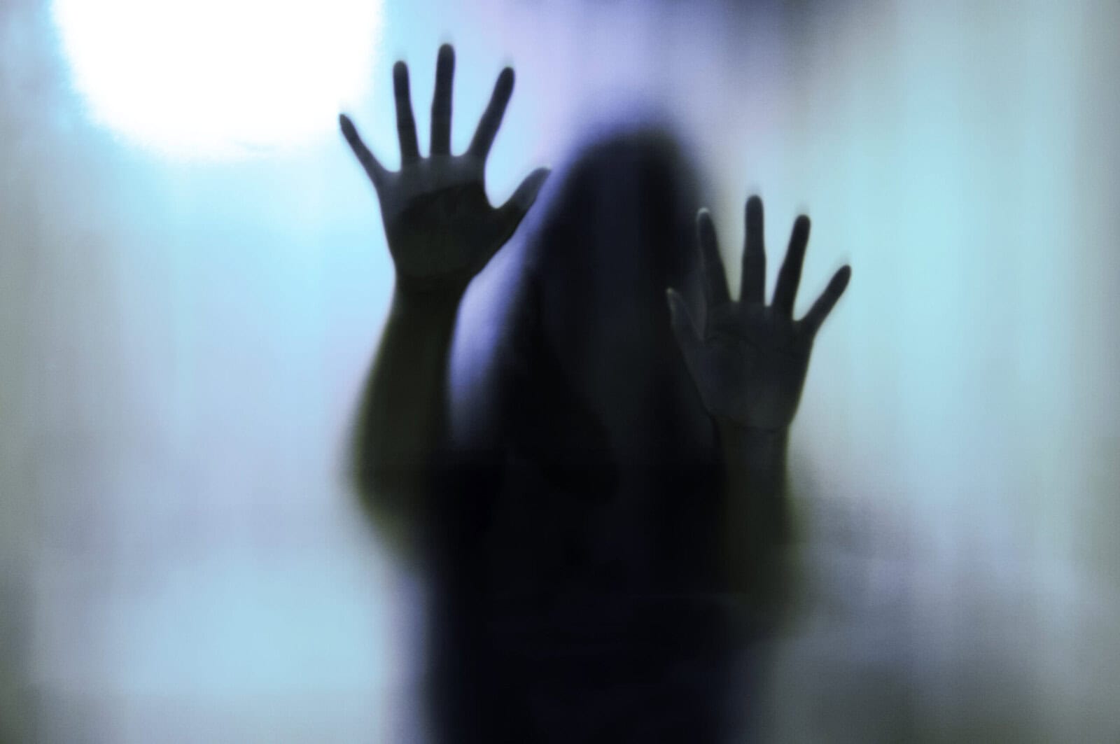 A blurry silhouette of Matt Fraser with outstretched hands pressed against a frosted glass surface, creating a mysterious and shadowy effect.
